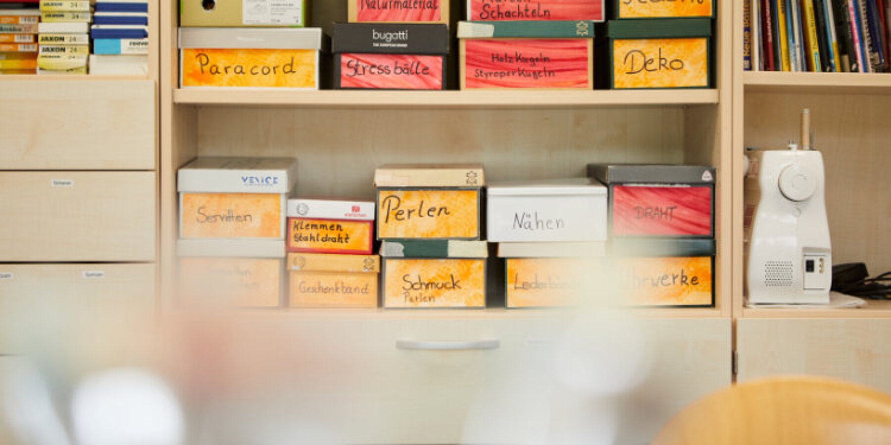 Blick in ein Holzregal mit beschrifteten Kartons und einer Nähmaschine