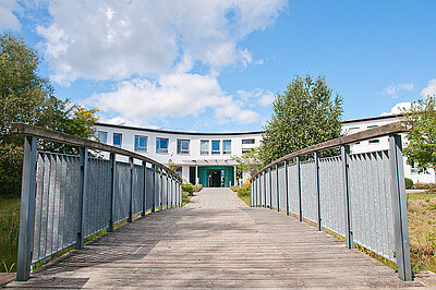 Panorama der Holzbrücke vor dem Haupteingang zur Psychiatrischen Klinik Uelzen, darüber blauer Himmel mit weißen Wolken