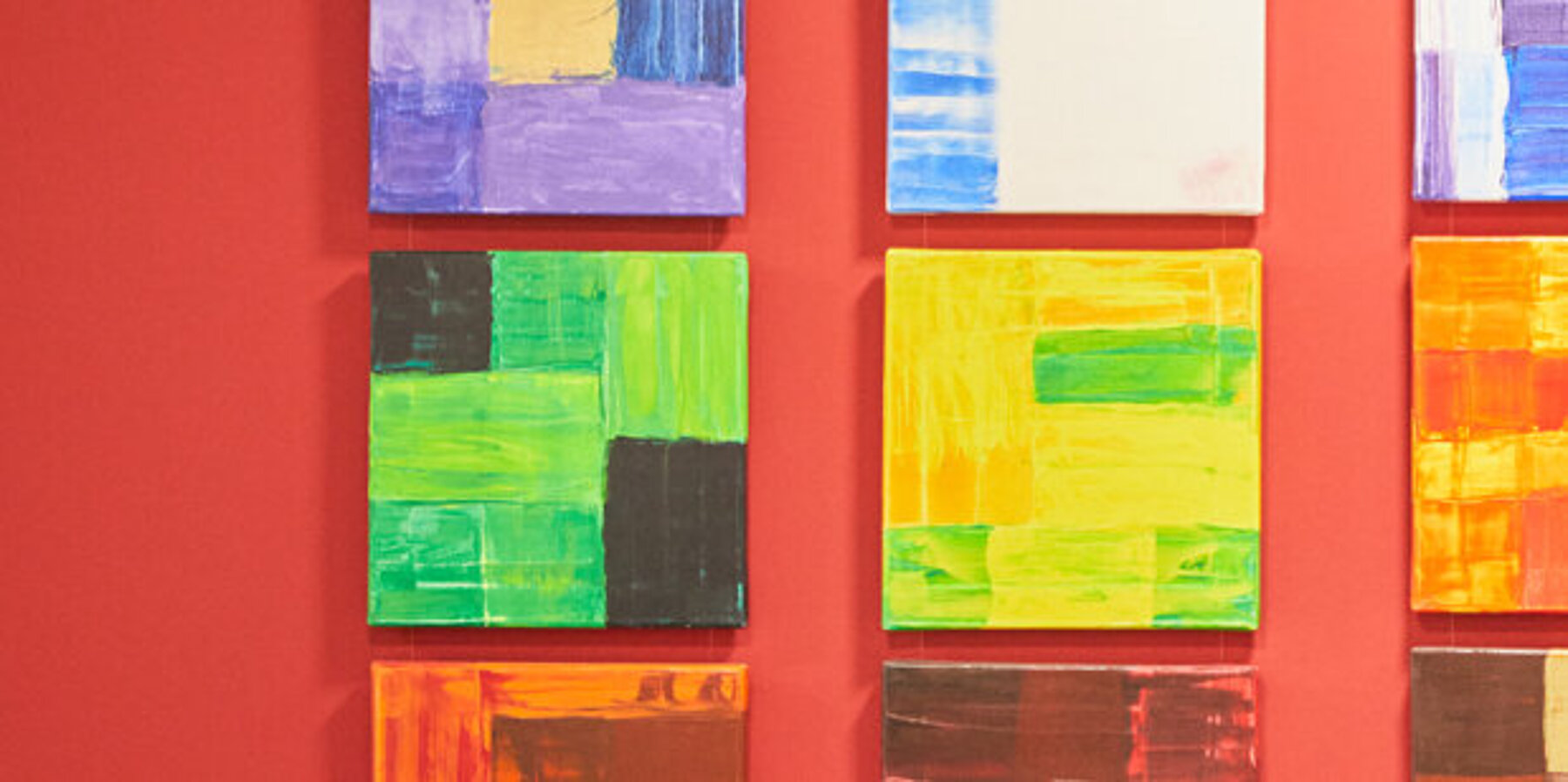Acht quadratische, bunte Bilder an einer roten Wand