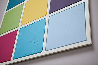 Detailaufnahme eines Wandbildes aus neun farbigen Quadraten an einer weißen Wand