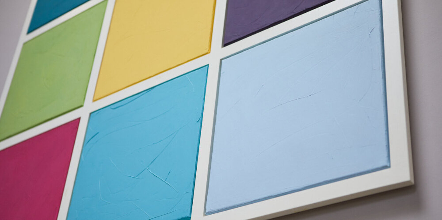 Detailaufnahme eines Wandbildes aus neun farbigen Quadraten an einer weißen Wand
