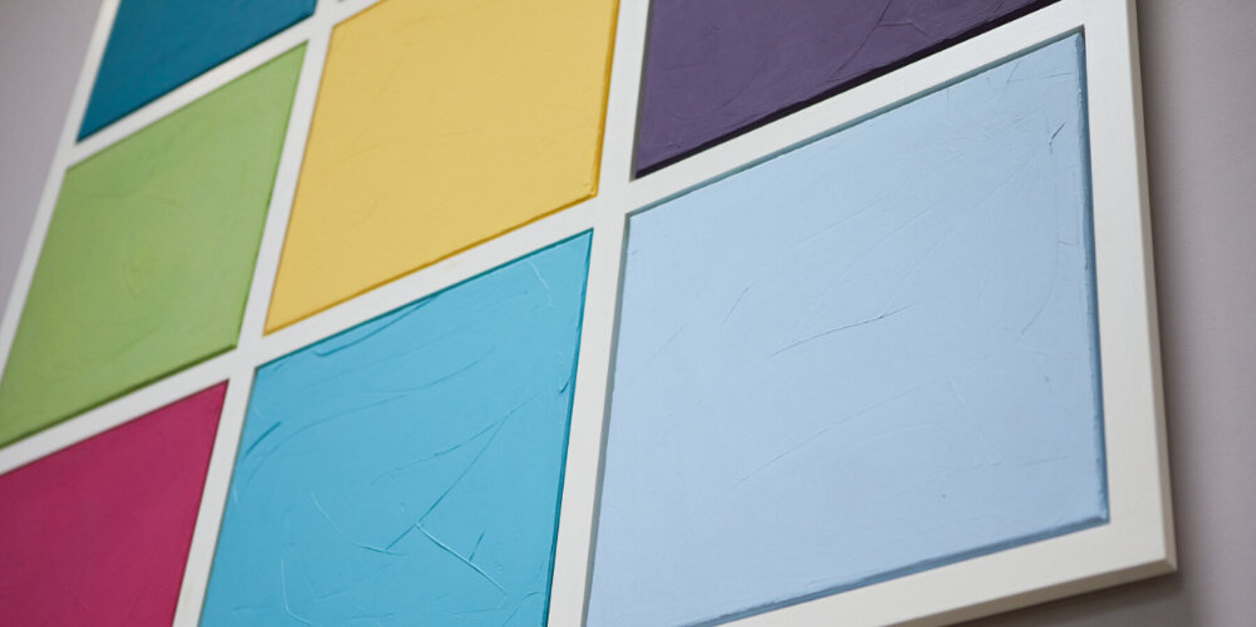 Detailaufnahme eines Wandbildes aus neun farbigen Quadraten an einer weißen Wand