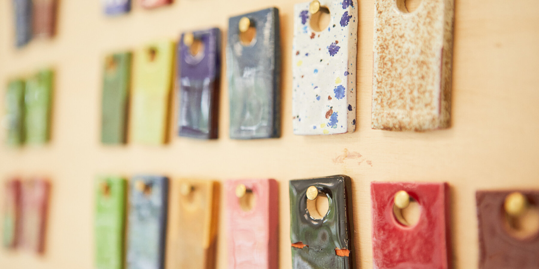 Kleine Rechtecke aus Ton, verschiedenfarbig bemalt, an kleinen Nägeln an einer Wand präsentiert