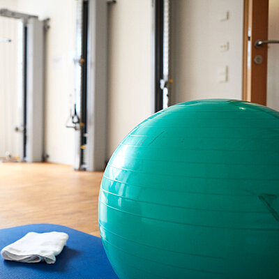 Bild aus einem Therapieraum: im Vordergrund ein großer grüner Gymnastikball, daneben eine Matte, auf der ein Handtuch liegt.