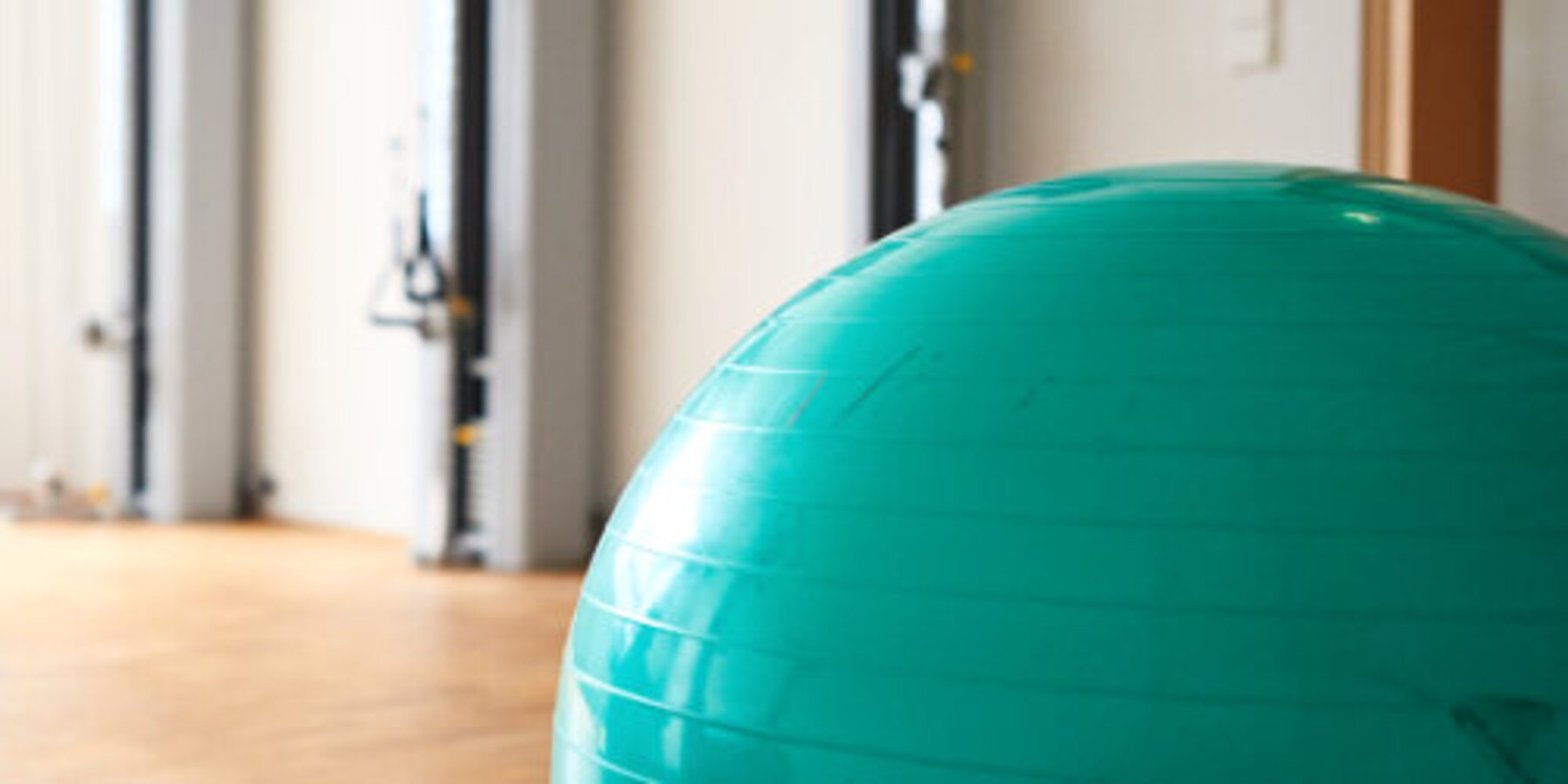 Bild aus einem Therapieraum: im Vordergrund ein großer grüner Gymnastikball, daneben eine Matte, auf der ein Handtuch liegt.